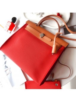 Bolso trapezoidal en lona y cuero rojo ladrillo, con candado dorado, asas planas y solapa refinada.